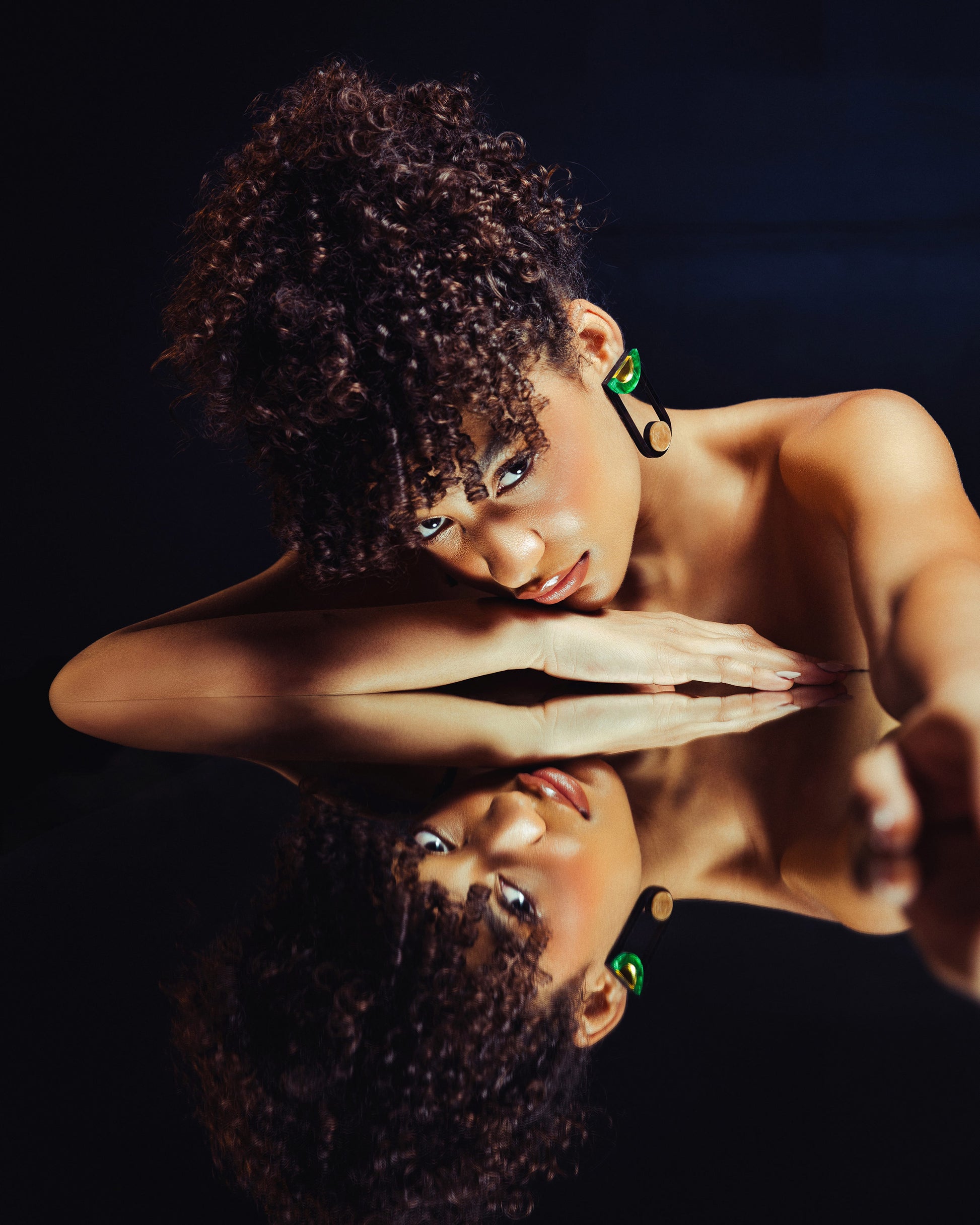 Woman with curly hair and green earrings looking at her reflection in a mirror.